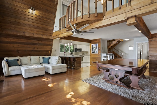 rec room with beam ceiling, high vaulted ceiling, ceiling fan, and wooden walls