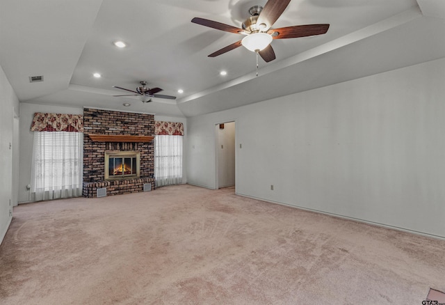 unfurnished living room with a brick fireplace, a wealth of natural light, light colored carpet, and a tray ceiling