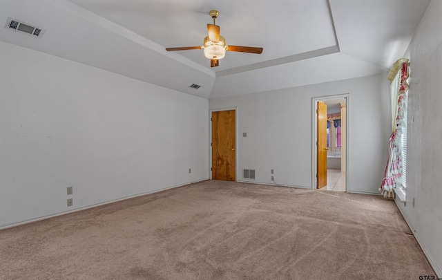 unfurnished bedroom with light carpet, a raised ceiling, vaulted ceiling, ceiling fan, and ensuite bathroom