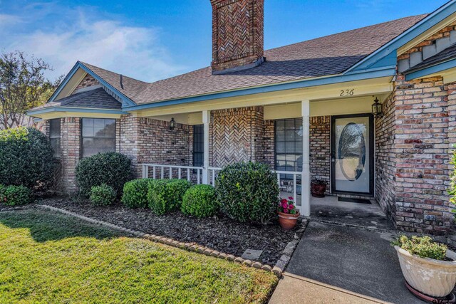 view of exterior entry featuring a yard and covered porch