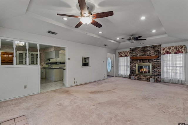 unfurnished living room featuring a brick fireplace, light colored carpet, ceiling fan, and a raised ceiling