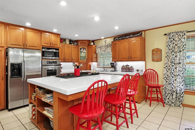 kitchen featuring light tile patterned flooring, appliances with stainless steel finishes, ornamental molding, a breakfast bar area, and a kitchen island