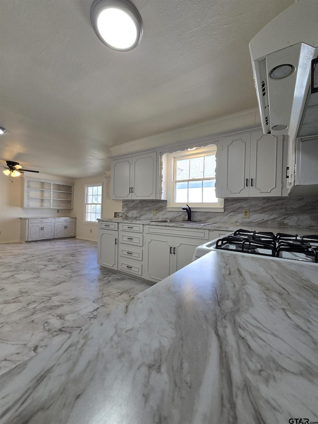 kitchen with ceiling fan, sink, backsplash, white cabinetry, and white gas range