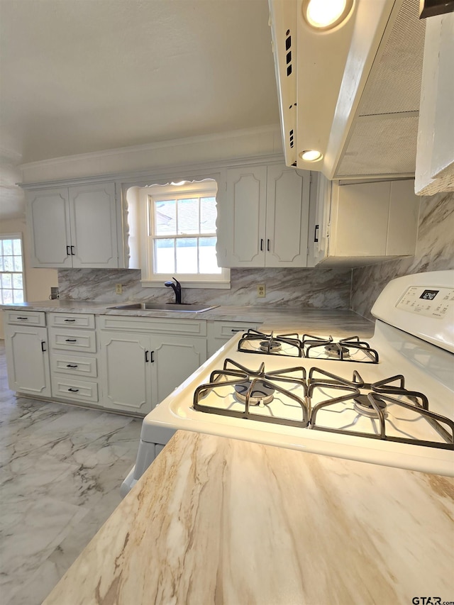 kitchen with range hood, white cabinets, sink, gas range gas stove, and ornamental molding