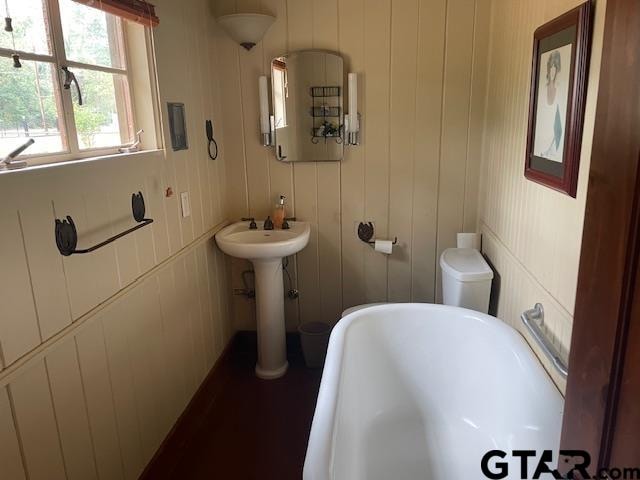 bathroom with sink, a bathtub, wooden walls, and water heater