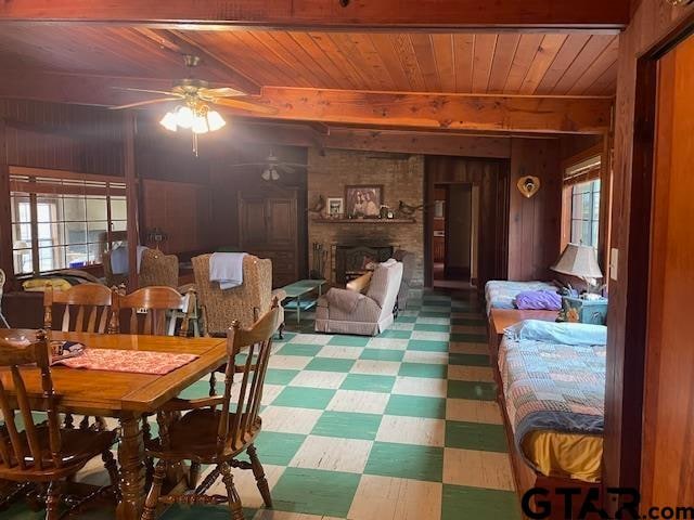 dining room featuring wooden ceiling, a brick fireplace, ceiling fan, and wooden walls