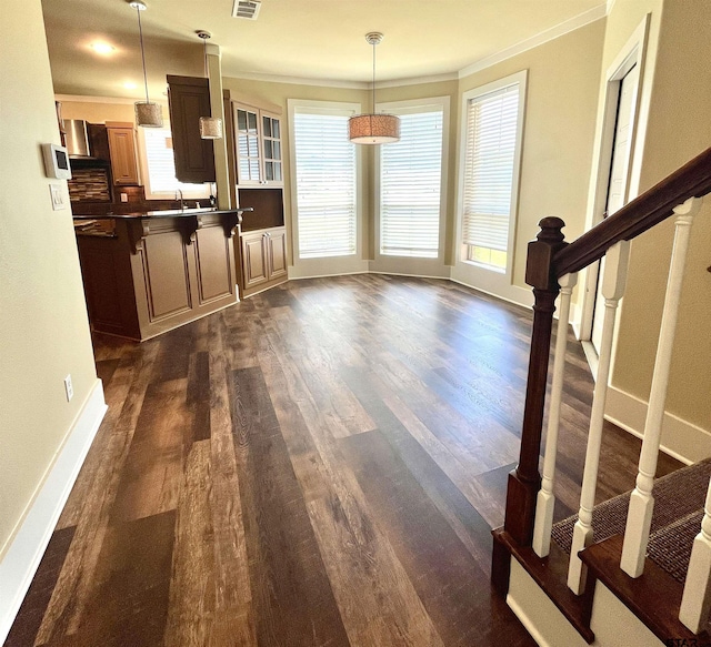 interior space featuring dark countertops, dark wood finished floors, ornamental molding, visible vents, and pendant lighting