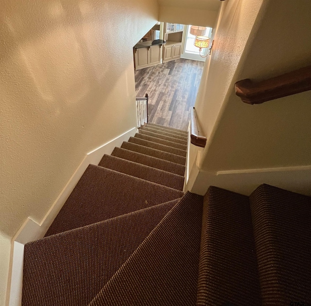 staircase with baseboards, a textured wall, and wood finished floors