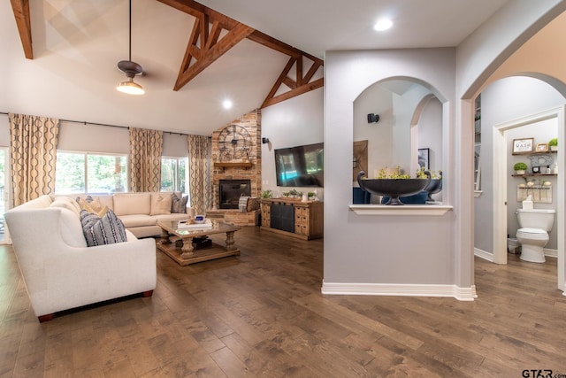 living room featuring beamed ceiling, wood-type flooring, a stone fireplace, and high vaulted ceiling