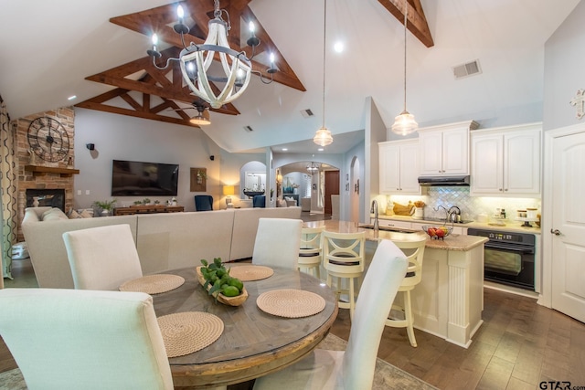 dining area with a notable chandelier, sink, dark hardwood / wood-style floors, beam ceiling, and a fireplace