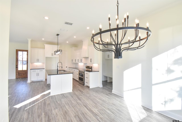 kitchen with decorative backsplash, white cabinets, an island with sink, and stainless steel range with electric stovetop