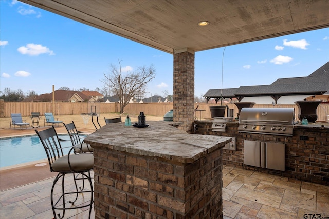 view of patio featuring grilling area, a fenced in pool, exterior kitchen, and exterior bar