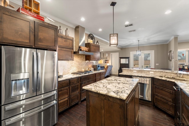 kitchen with a kitchen island, sink, light stone counters, appliances with stainless steel finishes, and wall chimney range hood