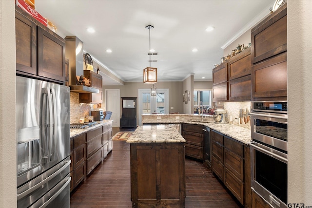 kitchen with hanging light fixtures, wall chimney exhaust hood, stainless steel appliances, a kitchen island, and kitchen peninsula