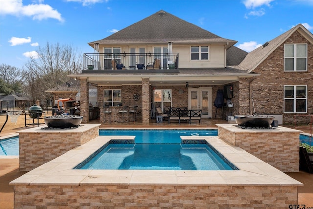 back of house with a patio area, an outdoor fire pit, a balcony, and a swimming pool with hot tub