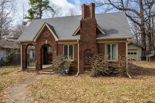 tudor home featuring an outdoor structure, brick siding, and a chimney