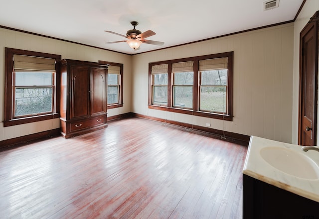 interior space with a sink, visible vents, wood finished floors, and ornamental molding