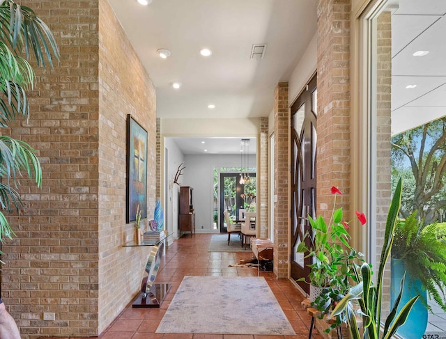 corridor featuring light tile patterned floors and brick wall