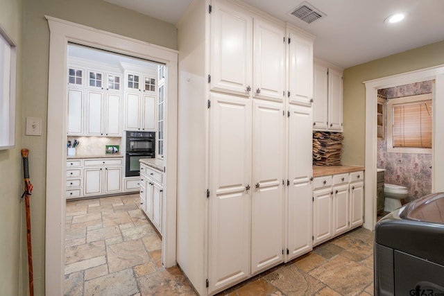 kitchen featuring white cabinets, black double oven, and decorative backsplash