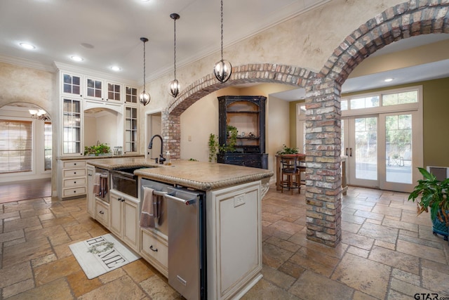 kitchen featuring sink, an island with sink, decorative columns, ornamental molding, and decorative light fixtures