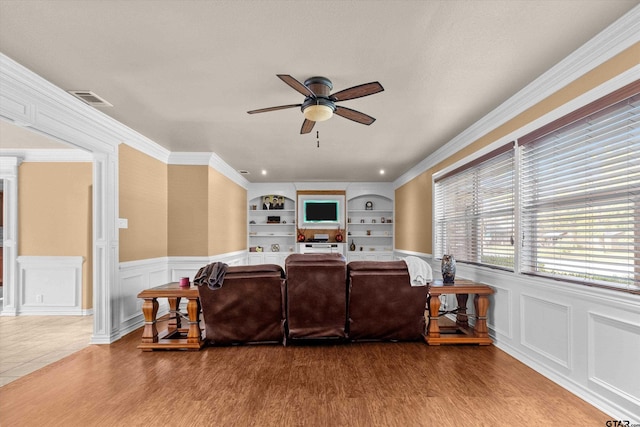 living room with built in shelves, hardwood / wood-style flooring, ceiling fan, and ornamental molding