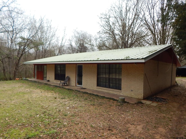 back of property with a yard, metal roof, and brick siding