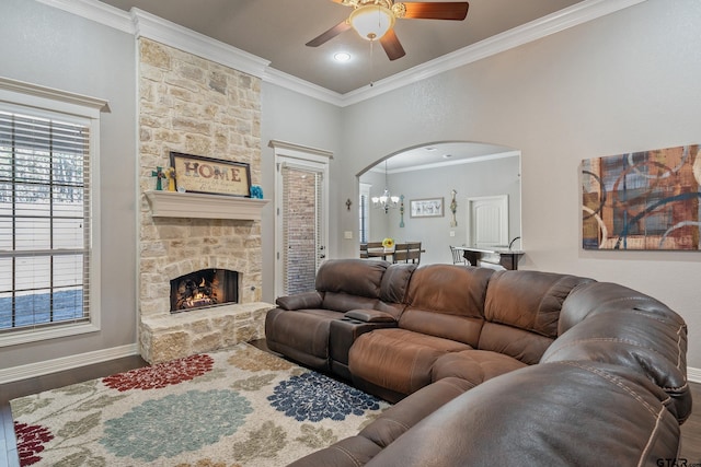 living room featuring crown molding, hardwood / wood-style floors, ceiling fan with notable chandelier, and a stone fireplace