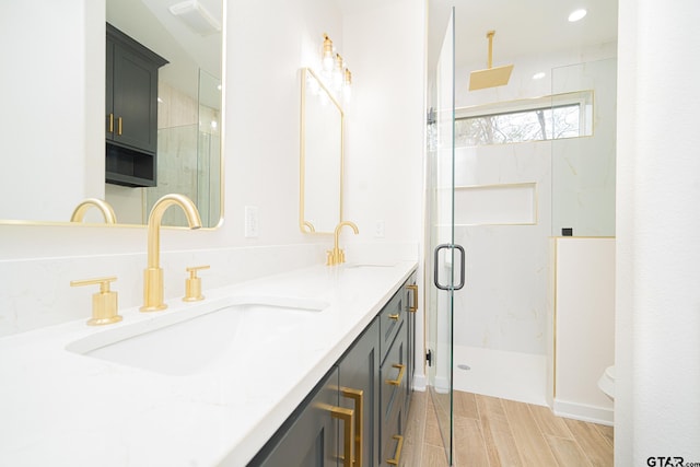 full bath featuring double vanity, a marble finish shower, wood finished floors, and a sink