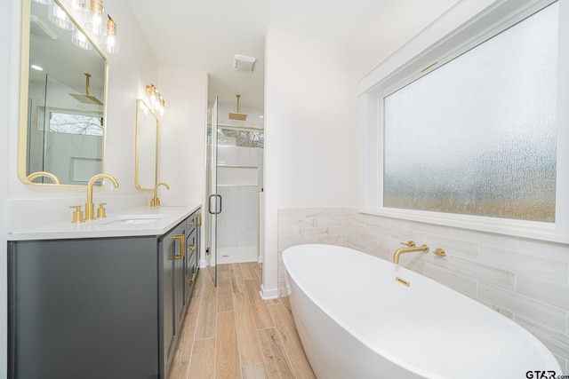 full bath with double vanity, a stall shower, a sink, tile walls, and a freestanding tub