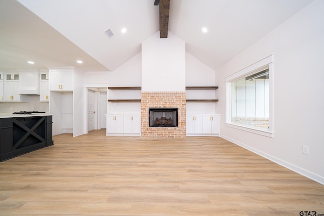 unfurnished living room with high vaulted ceiling, visible vents, light wood finished floors, a brick fireplace, and beamed ceiling