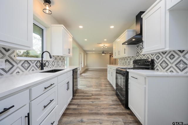kitchen with electric range, wall chimney range hood, white cabinetry, and a sink