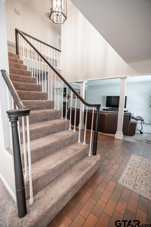 stairway with ornate columns, a notable chandelier, and a textured ceiling