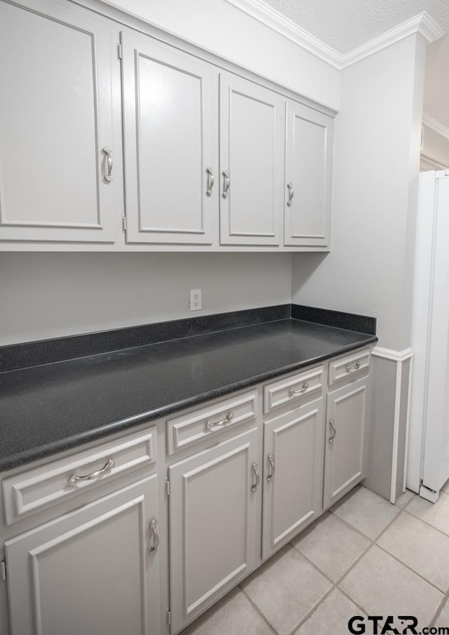 kitchen with light tile patterned flooring, a textured ceiling, crown molding, gray cabinets, and white refrigerator