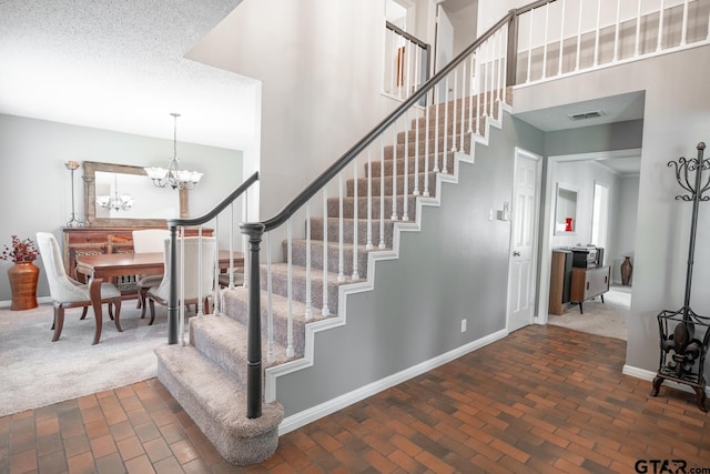 staircase featuring a high ceiling, a textured ceiling, and an inviting chandelier