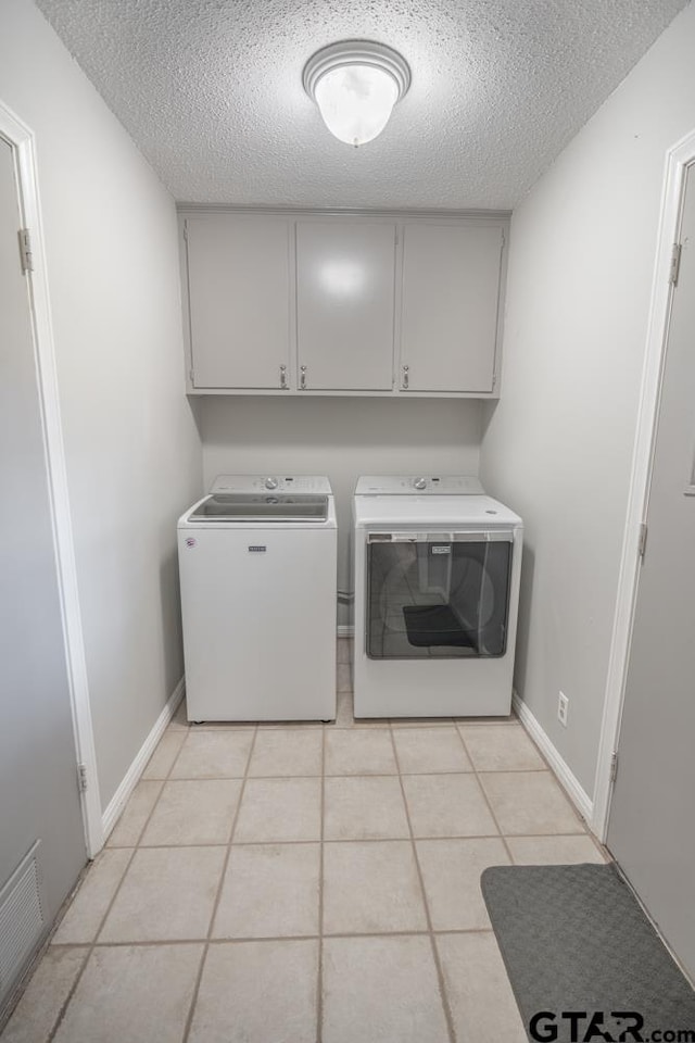 clothes washing area with cabinets, washing machine and dryer, a textured ceiling, and light tile patterned floors