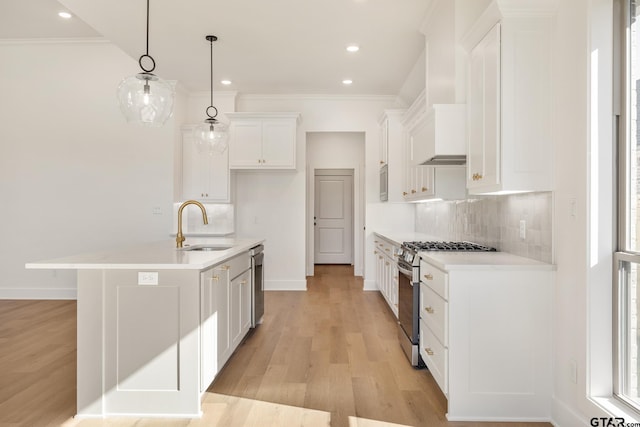 kitchen with a kitchen island with sink, white cabinets, sink, hanging light fixtures, and stainless steel appliances