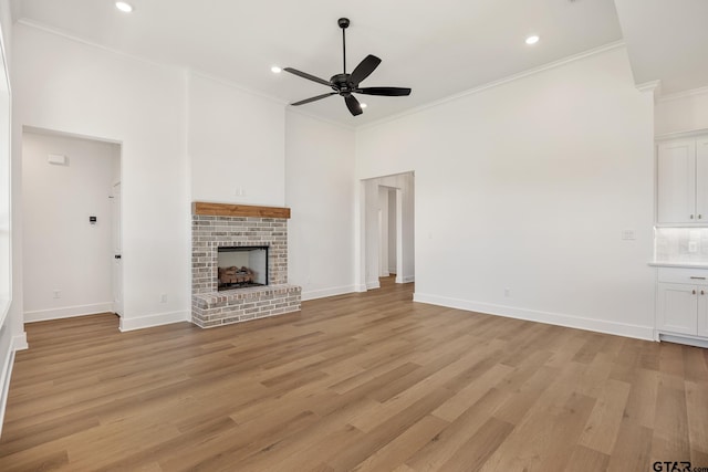 unfurnished living room featuring ceiling fan, light wood-type flooring, crown molding, and a brick fireplace