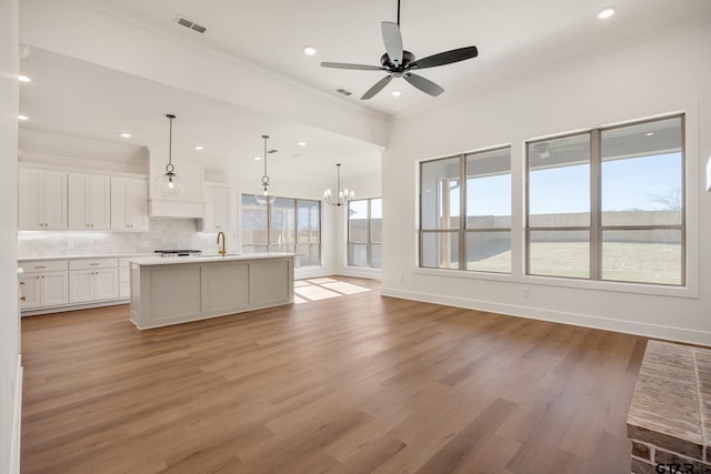 kitchen featuring a kitchen island with sink, hanging light fixtures, decorative backsplash, light wood-type flooring, and white cabinetry