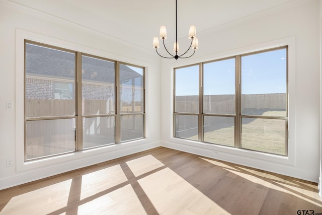 unfurnished dining area with a healthy amount of sunlight, crown molding, a chandelier, and wood-type flooring