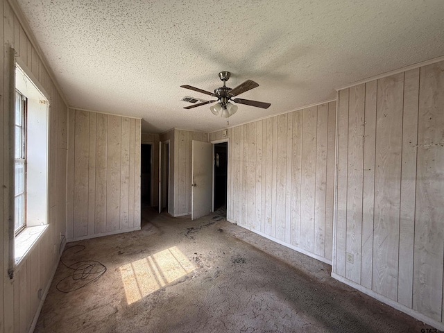 spare room featuring visible vents, a ceiling fan, wood walls, and a textured ceiling