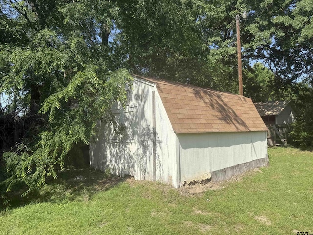 view of side of home featuring a gambrel roof, a shed, an outdoor structure, a yard, and roof with shingles