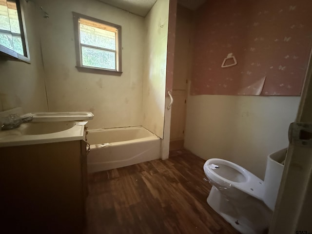 bathroom with a tub to relax in, wood finished floors, toilet, and vanity