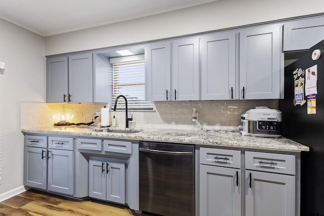 kitchen with sink, black refrigerator, light stone counters, decorative backsplash, and light wood-type flooring