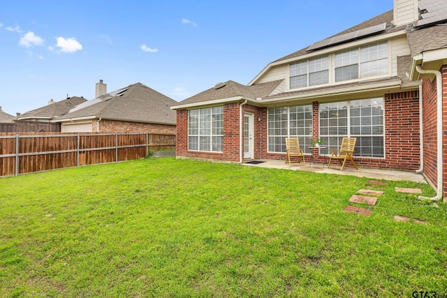 rear view of property with a fenced backyard, roof with shingles, brick siding, a patio area, and a yard