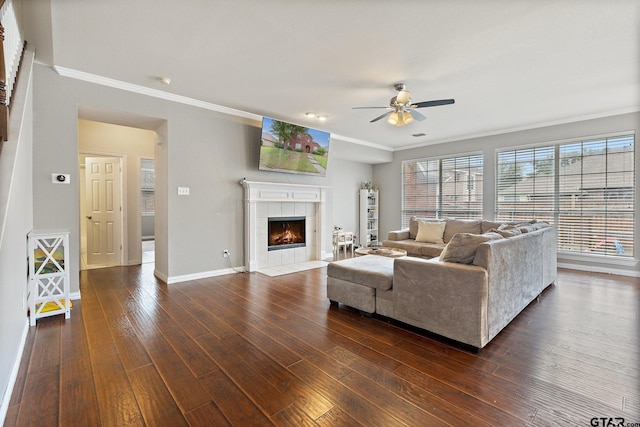 living room featuring a fireplace, a ceiling fan, baseboards, dark wood-type flooring, and ornamental molding