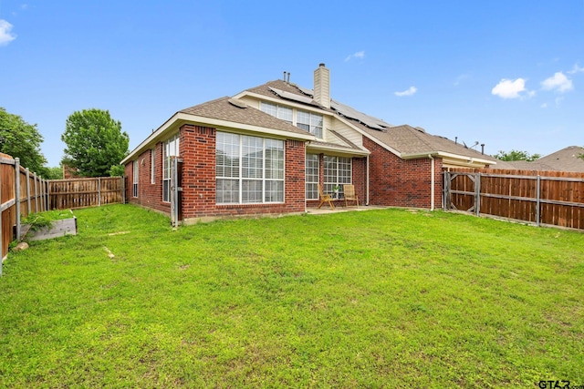 rear view of property with a fenced backyard, a chimney, brick siding, a lawn, and solar panels