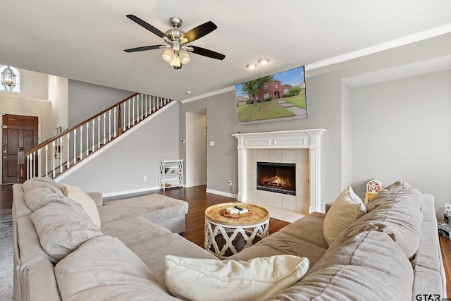living room with a tiled fireplace, stairs, a ceiling fan, baseboards, and wood finished floors