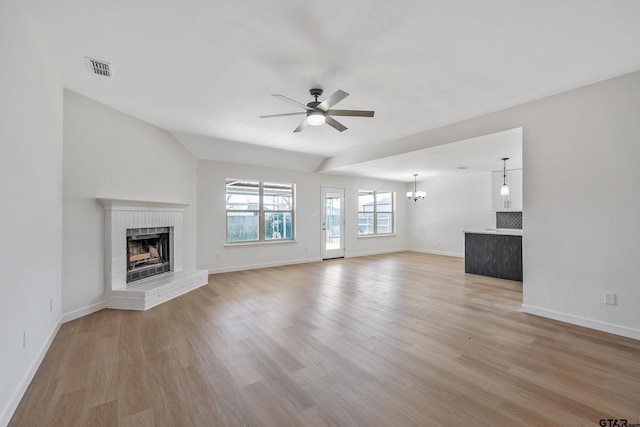 unfurnished living room featuring lofted ceiling, ceiling fan with notable chandelier, a fireplace, and light hardwood / wood-style flooring