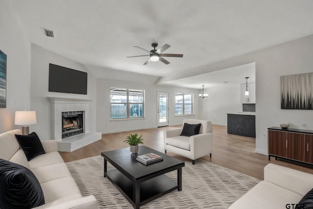 living room with baseboards, a brick fireplace, light wood-style flooring, and ceiling fan with notable chandelier