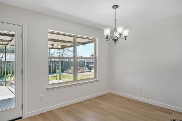 unfurnished dining area featuring an inviting chandelier, a wealth of natural light, and light wood-type flooring